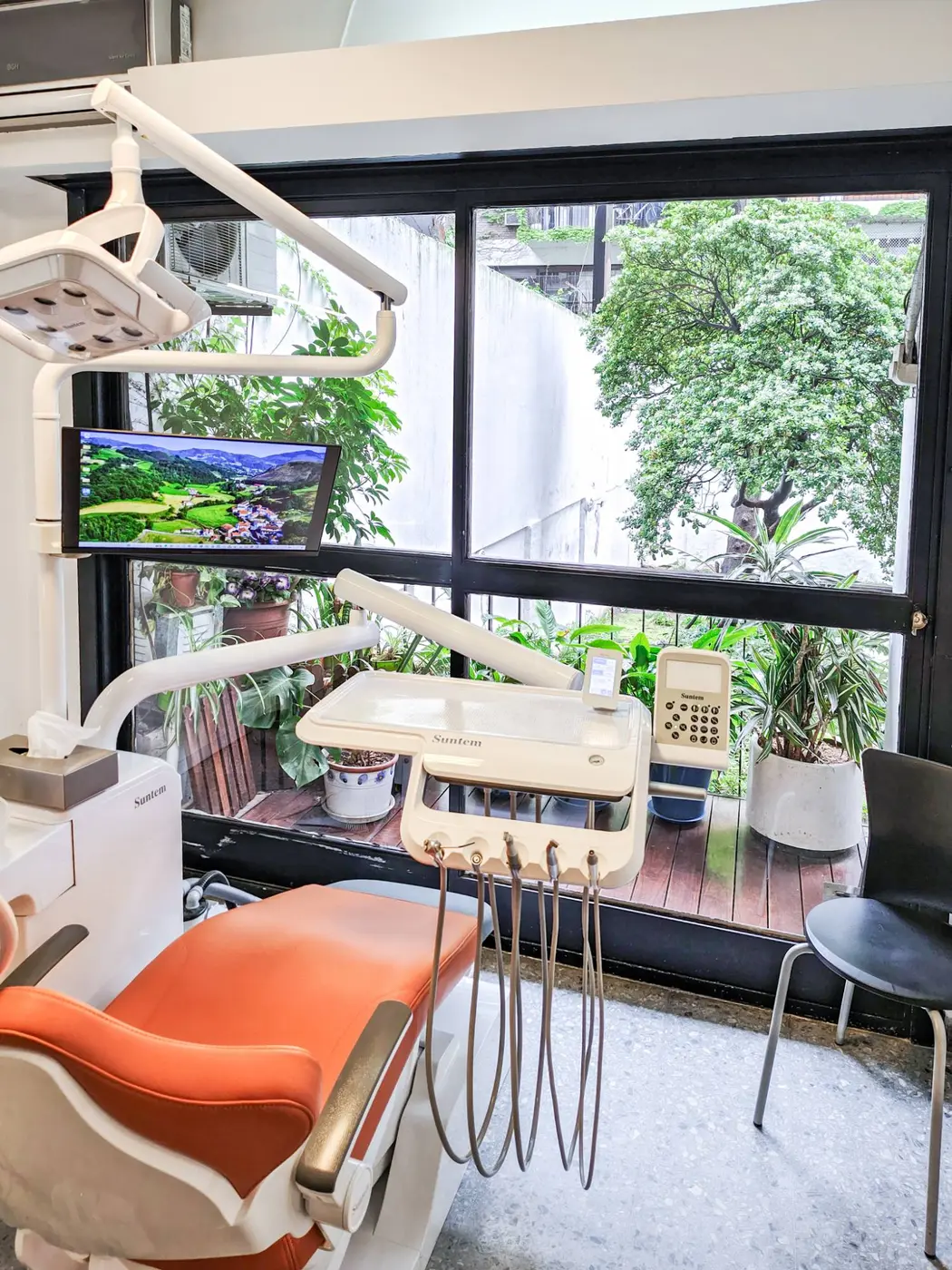 Sillón odontológico naranja con monitor y ventanal sobre el balcón con plantas